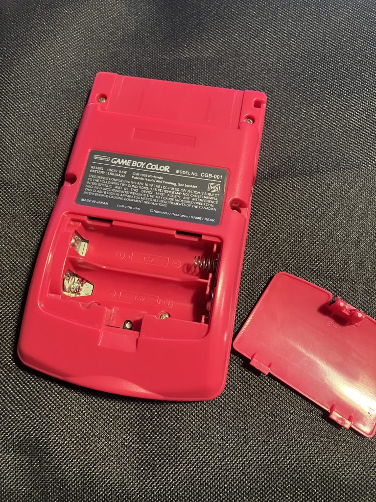 A Game Boy with the battery cover removed. There are no batteries installed.