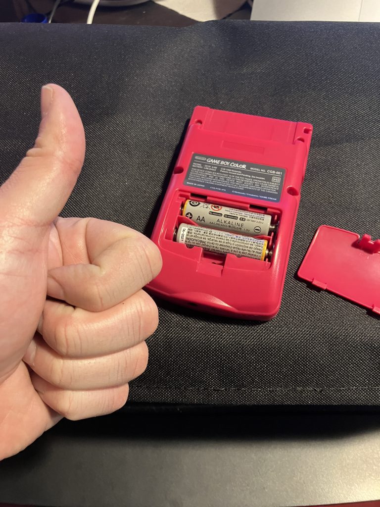A Game Boy with 2 AA batteries installed. A hand giving the "thumbs up" gesture is in front.